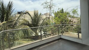 A balcony with a metal railing, palm trees, and buildings in the background.