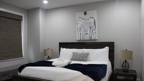 Un dormitorio con una cama grande, dos lámparas de noche, una ventana con persianas y una obra de arte abstracta en la pared.