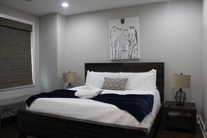 Ein Schlafzimmer mit einem großen Bett, zwei Nachttischlampen, einem Fenster mit Jalousien und einem abstrakten Kunstwerk an der Wand.