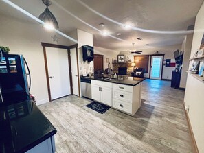 Una cocina moderna con una isla central, un comedor con chimenea y una sala de estar con televisor y una bandera.