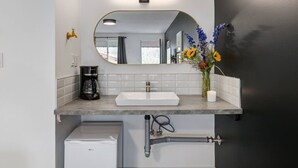 A modern bathroom with a white sink, a coffee maker, a mirror, and a vase with flowers. - Gateway Suites: Charming Stay Perfect for 4 Guests! (Harvie Heights)