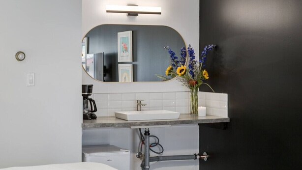 A modern bathroom with a white sink, a mirror, and a vase of sunflowers. - Gateway Suites: Charming Stay Perfect for 4 Guests! (Harvie Heights)