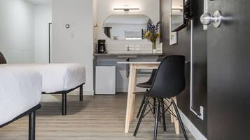 Habitación de hotel pequeña con cama, kitchenette, zona de comedor con silla y espejo.
