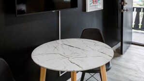A round table with a marble top, a black chair, a mounted flat-screen TV, and a door with a glass panel. - Gateway Suites: Charming Stay Perfect for 4 Guests! (Harvie Heights)