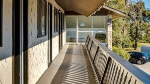 A covered outdoor area with a wooden deck, a metal railing, and a view of a parked car and trees. - Gateway Suites: Charming Stay Perfect for 4 Guests! (Harvie Heights)