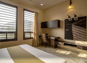Ein Hotelzimmer mit Bett, Schreibtisch, Stuhl, Fernseher und einem Fenster mit Vorhängen.