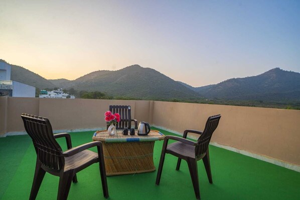 A rooftop terrace with a table set for two, chairs, and a view of mountains. - TGC VILLA (Udaipur)
