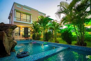 A modern house with a swimming pool, surrounded by tropical plants and a large rock feature. - TGC VILLA (Udaipur)