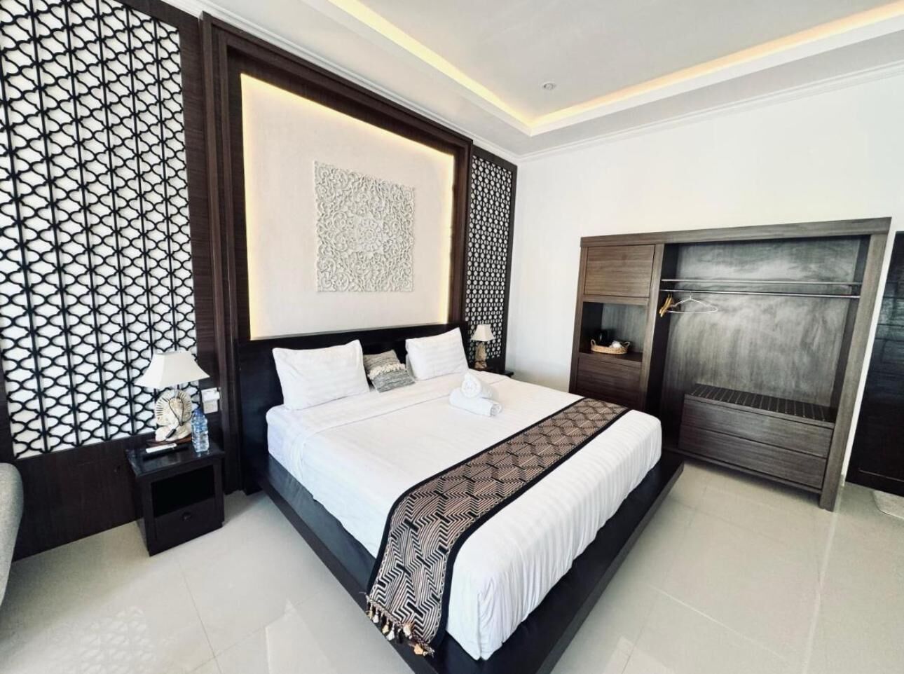 A modern bedroom with a large bed, a dark wooden headboard, a decorative wall panel, and a built-in wardrobe.