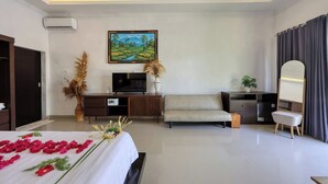 A modern hotel room with a bed, a sofa, a desk, a TV, and a large painting on the wall. - Kelingking Mesari Villa & Spa (Penida Island)