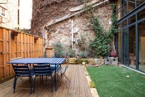 A patio with a table and chairs, a wooden deck, a stone wall, and a small grassy area.