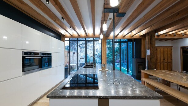 A modern kitchen with a central island, built-in ovens, and a large window overlooking a garden.
