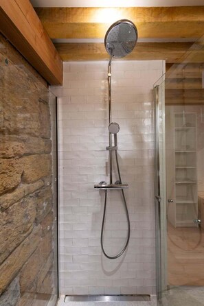 A shower with a glass door, a stone wall to the left, and a wooden ceiling.