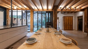A modern kitchen with a long wooden table set for dining, large windows, and a view of the outdoors.