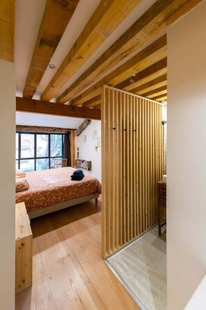 A wooden-framed room with a bed, a window, and a wooden partition.