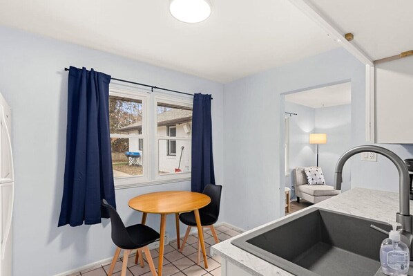 A compact room with a dining table and chairs, a sink, and a window with curtains.