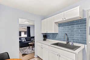 A compact kitchen with white cabinets, a blue-tiled backsplash, and a sink.