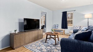 Un salon moderne avec un téléviseur à écran plat posé sur un meuble en bois, une table basse ronde, un canapé bleu, un tapis à motifs et une lampe sur pied.