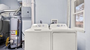 Une buanderie équipée d’un chauffe-eau, de deux sèche-linge et d’une fenêtre.