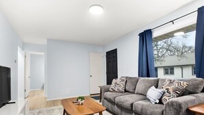 Un salon moderne avec un canapé gris, une table basse en bois et un téléviseur posé sur un meuble blanc.