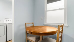 Quarto nos fundos com uma mesa redonda de madeira e cadeiras, uma janela e espaço para lavanderia com máquinas de lavar.