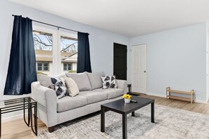 Un salon avec un canapé gris, une table basse noire et une fenêtre ornée de rideaux foncés.