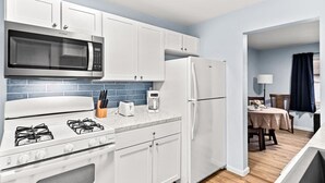 A compact kitchen with white cabinets, a microwave, a stove, and a refrigerator.