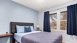 A bedroom with a bed, a nightstand, a lamp, and a window with curtains.
