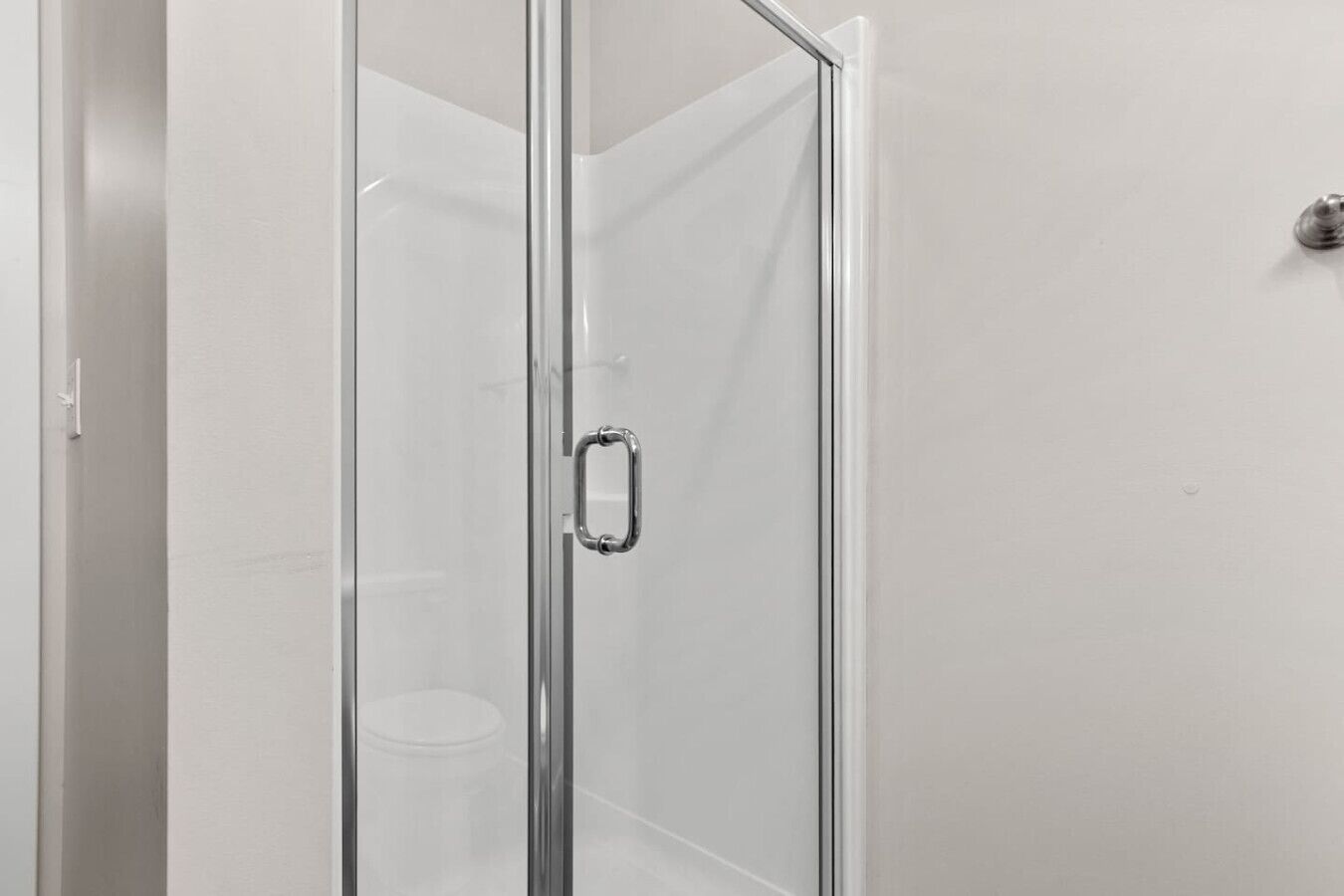 A glass-enclosed shower stall with a metal handle.