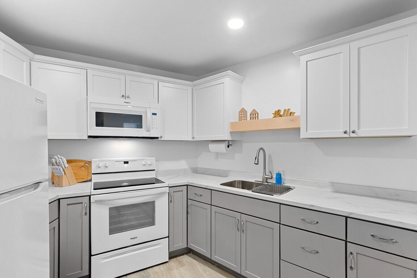 A modern kitchen with white cabinets, a microwave, a stove, and a sink.