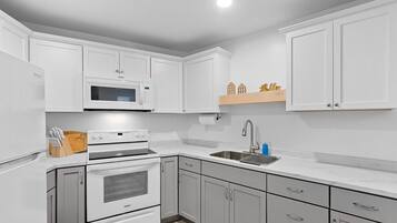 A modern kitchen with white cabinets, a microwave, a stove, and a sink.