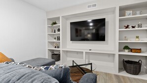 Un salon moderne avec un téléviseur à écran plat fixé au mur, un canapé gris et une table basse en verre.
