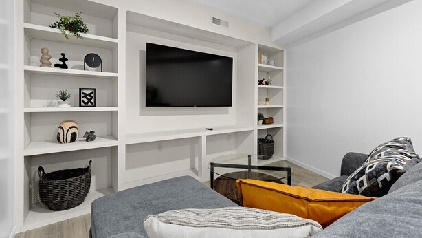 Un salon moderne avec un téléviseur à écran plat fixé à un mur blanc, entouré d’étagères où sont disposés divers objets décoratifs.
