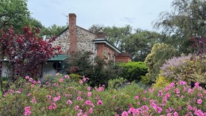 Un edificio in pietra con tetto verde, circondato da cespugli fioriti rosa e diversi alberi.
