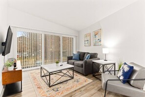 Una sala de estar moderna con sofá, sillón, mesa de centro y televisor sobre un mueble.
