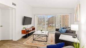 Ein modernes Wohnzimmer mit Flachbildfernseher, einer Couch, einem Couchtisch und Blick durch große Fenster nach draußen.