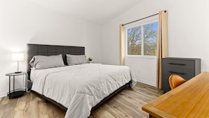 Ein Schlafzimmer mit Bett, Nachttisch, Lampe, Schreibtisch und Fenster.