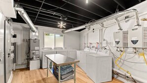 Ein Waschraum mit vier Waschmaschinen, einem Tisch und sichtbarer Sanitär- und Elektroinstallation.