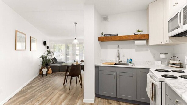 Une cuisine moderne avec des meubles gris, une cuisinière blanche et un plan de travail en bois.