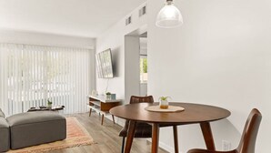 Un salon moderne avec une table de salle à manger ronde en bois, des fauteuils en cuir, un canapé gris et un plancher en bois.