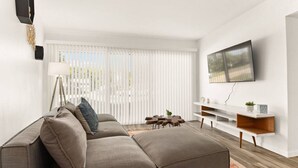 Un salon moderne avec un canapé d’angle, un téléviseur à écran plat fixé au mur et une console au design minimaliste.
