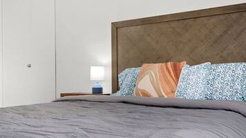 A neatly made bed with a grey comforter and patterned pillows, a bedside table with a lamp, and a wooden headboard.
