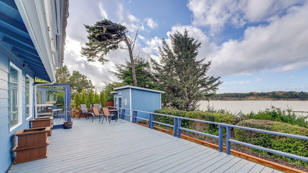 Une terrasse en bois avec des meubles d’extérieur, un petit abri de jardin et une vue sur un lac.