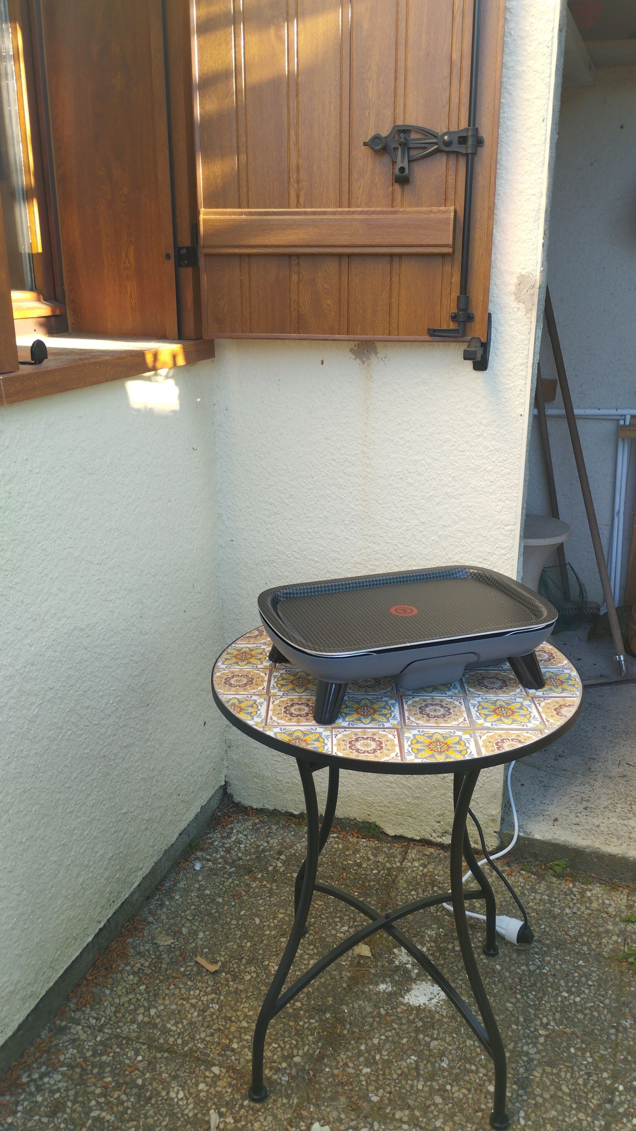 A small outdoor table with a tray, a wooden cabinet above, and a tiled floor.