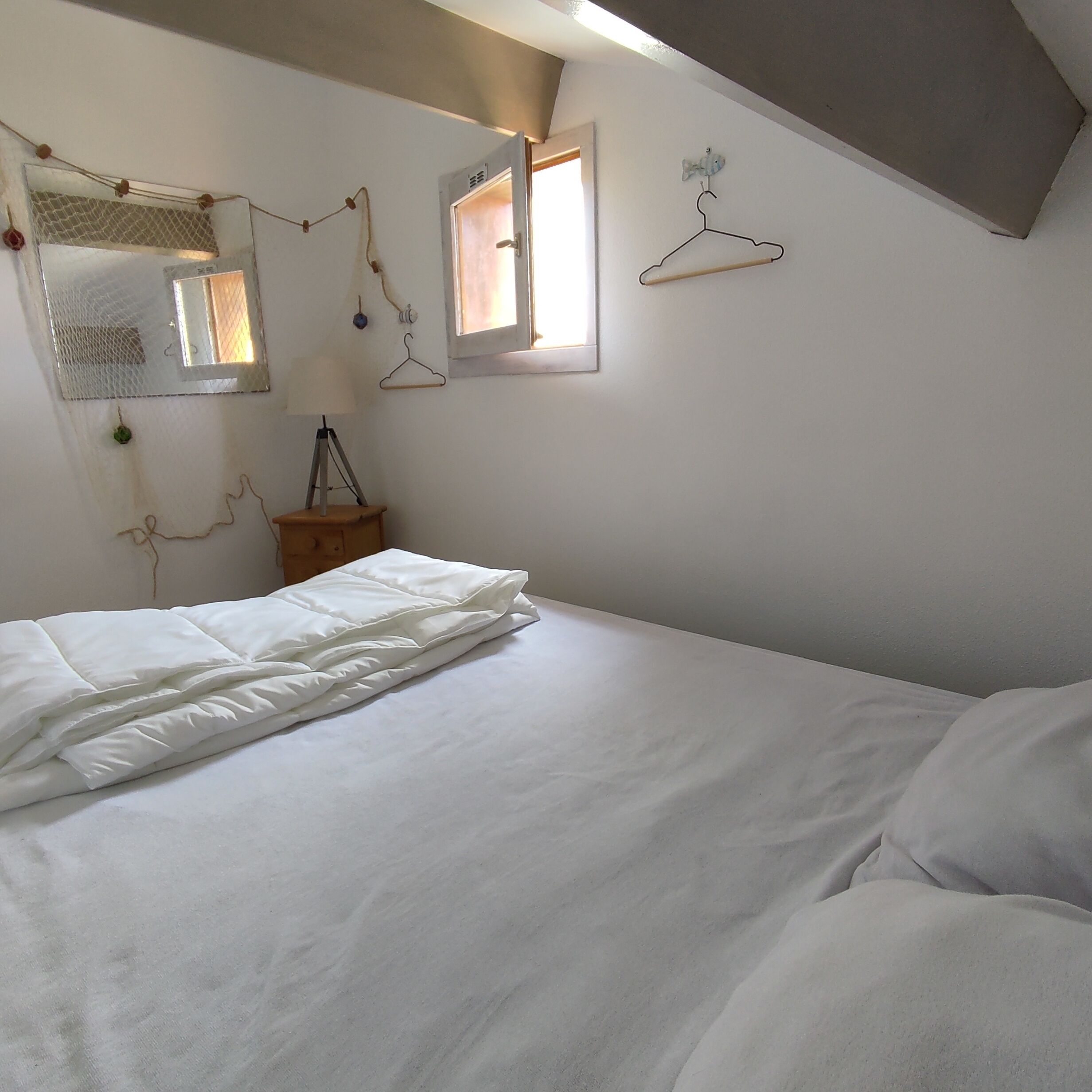 A bedroom with a bed, a hanging light, a window, and a wall-mounted hanger.