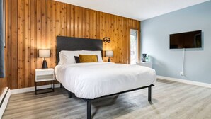 Un dormitorio moderno con un panel de madera en la pared, una cama grande con ropa blanca, dos mesitas de noche con lámparas y un televisor de pantalla plana montado en la pared.