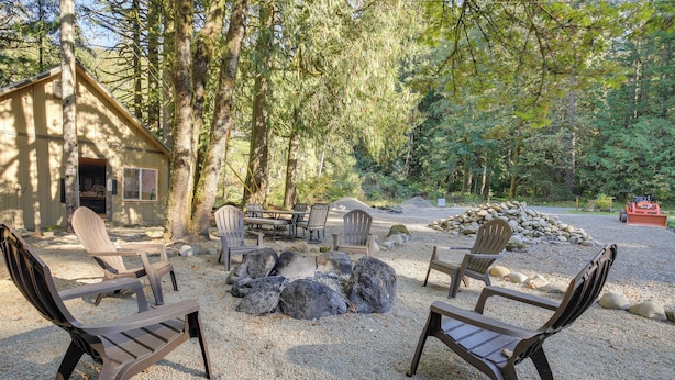 Uma cabana com um braseiro rodeado por cadeiras Adirondack, localizada numa área arborizada.