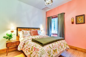 A bedroom with a floral bedspread, a bedside table with a plant, a nightstand, a window with curtains, and a wall-mounted light fixture. - Retro Rhododendron Retreat! Mt Hood Cabin (Rhododendron)