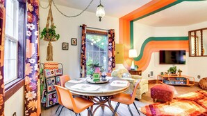 Uma sala de jantar com uma mesa redonda, cadeiras laranja e uma planta de macramé pendurada.