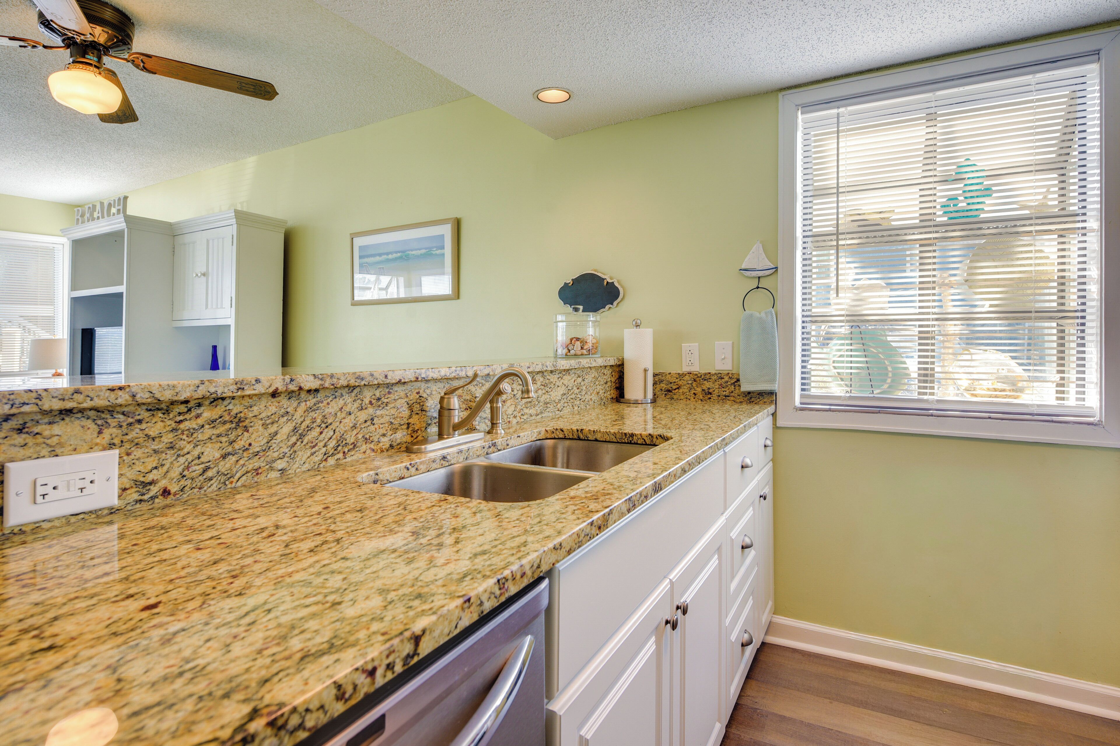 A kitchen with granite countertops, white cabinets, a double sink, and a ceiling fan.